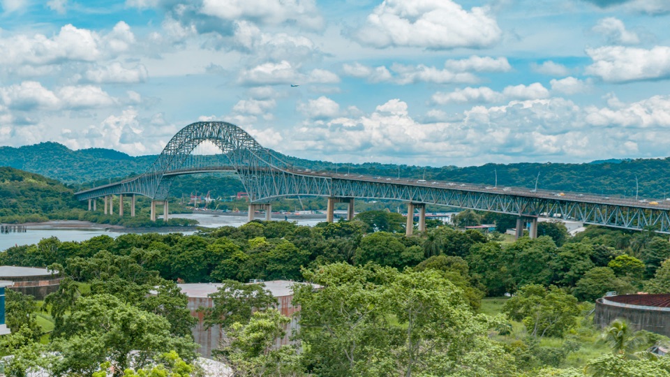 El Puente de las Américas con su arco de acero sobre la entrada del Canal, cerros verdes detrás y el bosque delante